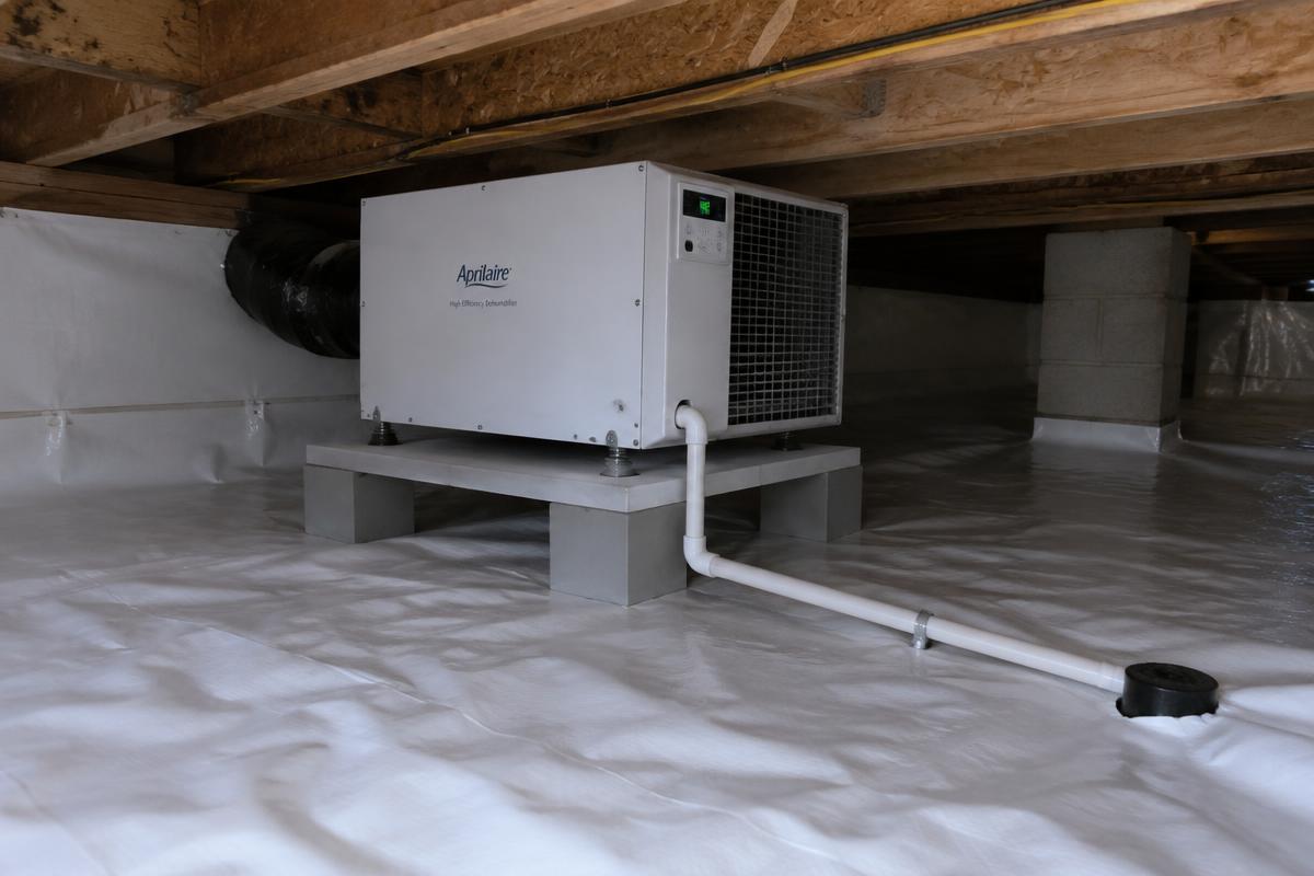 Crawl space dehumidifier installed on a raised platform with a condensate drain line